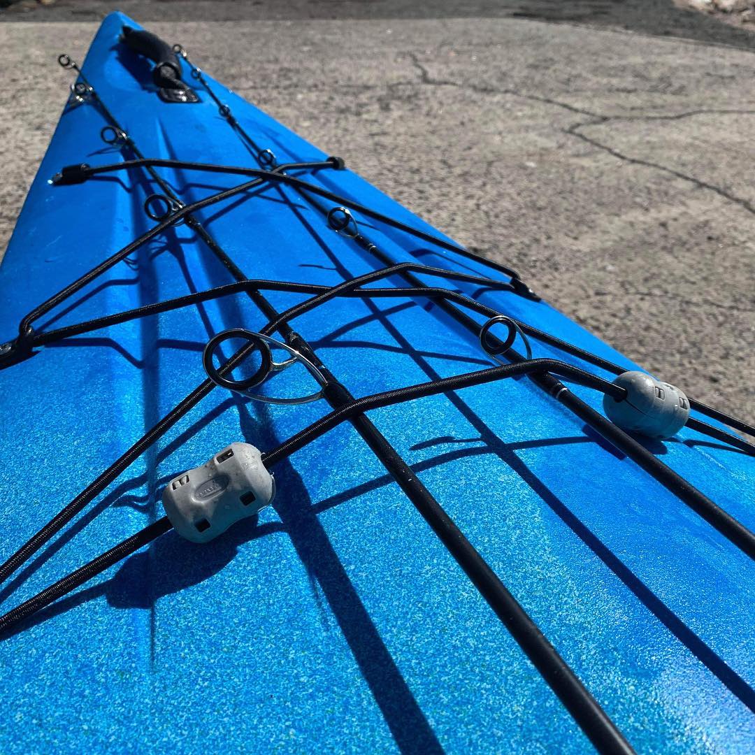 Surf-ready rod stowage system on the front of a viking profish reload kayak, showing rods flattened under toggles and bungee straps.