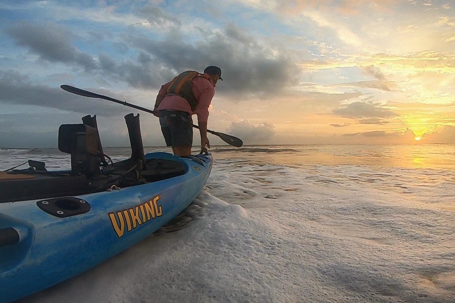 Angler launching a viking kayak into the surf at sunrise