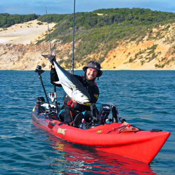 Angler holding a large tuna on a red fishing kayak during a sunshine coast adventure.